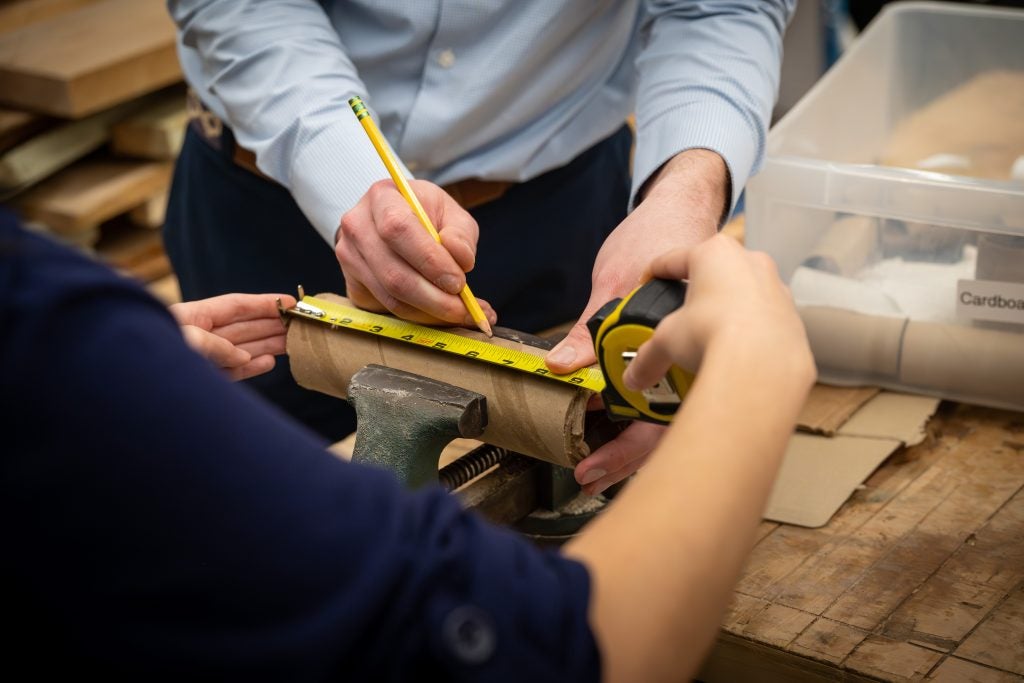 Two students measure the width of a cardboard roll.
