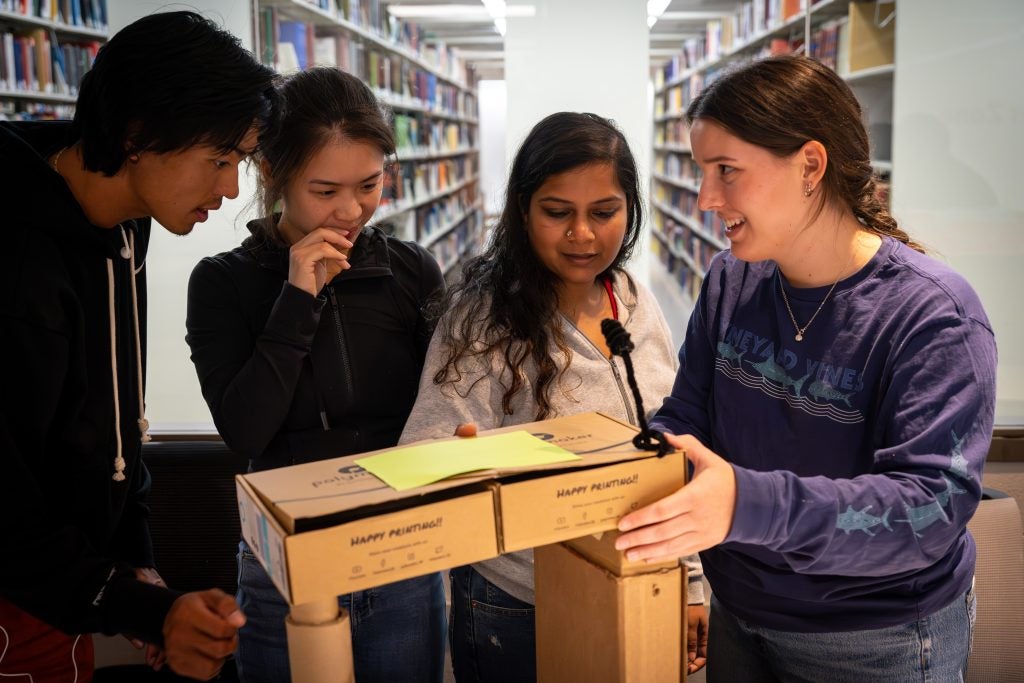 A group of students huddle around a cardboard mock-up of an accessible podium