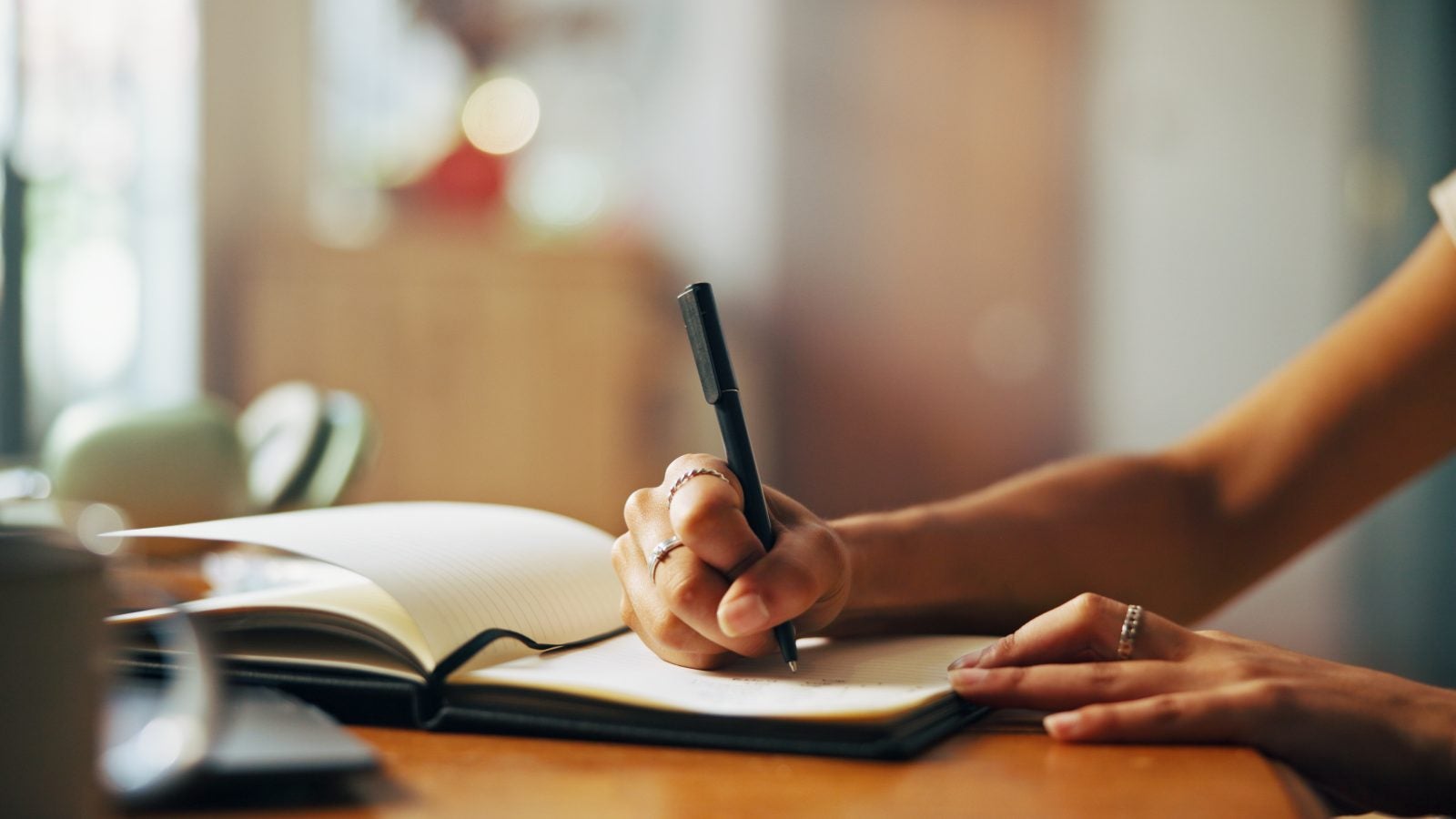 Home, person and hands with notebook for writing, schedule or daily reflection for wellness. Closeup, writer and student with journal