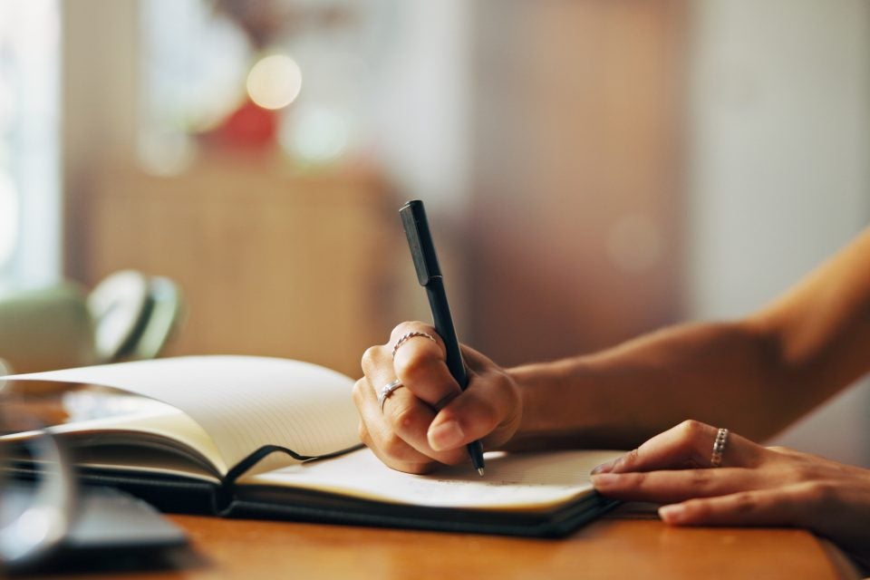Home, person and hands with notebook for writing, schedule or daily reflection for wellness. Closeup, writer and student with journal