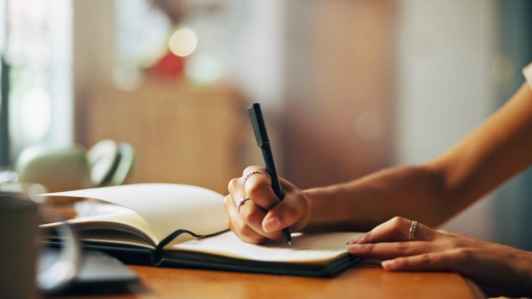 Home, person and hands with notebook for writing, schedule or daily reflection for wellness. Closeup, writer and student with journal