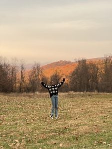 Young Black woman with arms raised up for a photo on a mountainside during sunset