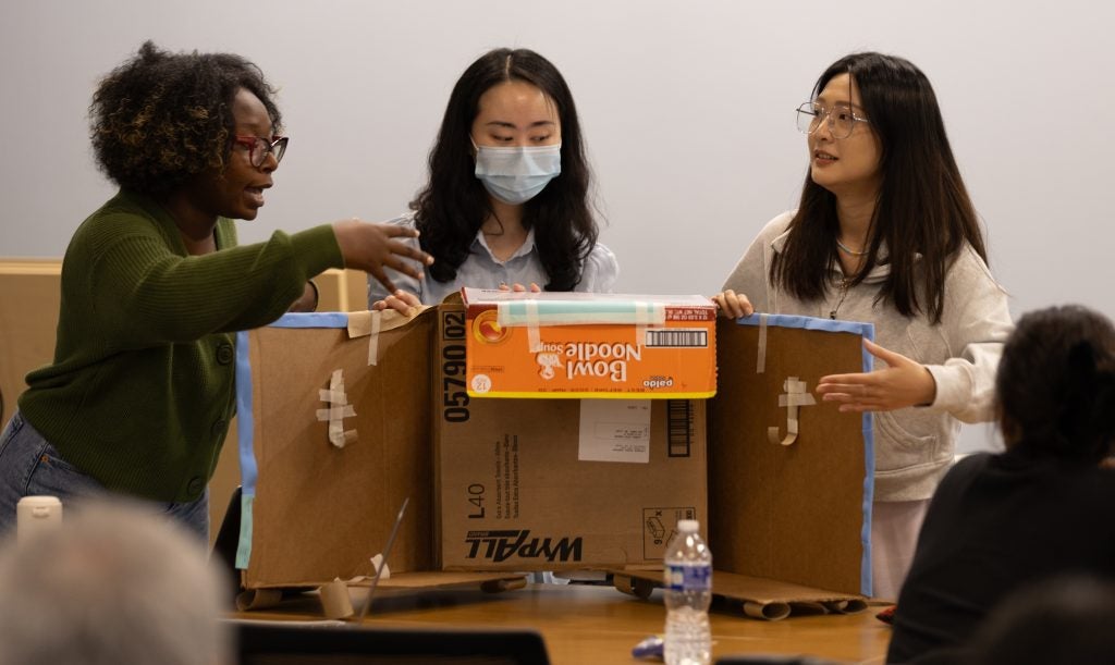Three students present a cardboard prototype of an accessible podium with wings that swing out.