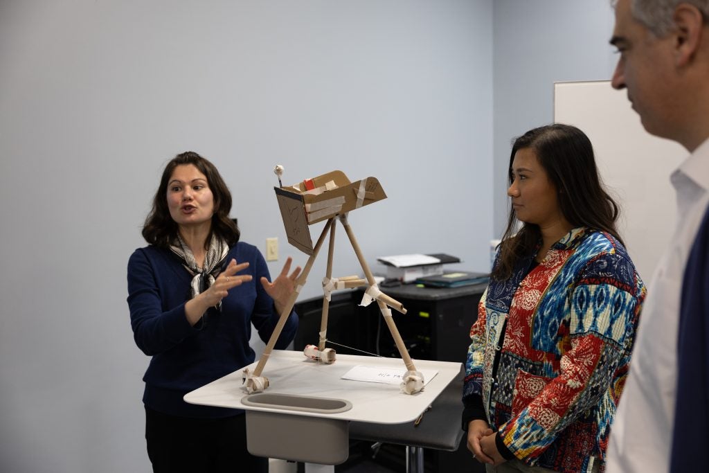 Three students present a cardboard mock-up of an accessible podium that was inspired by a camera tripod.