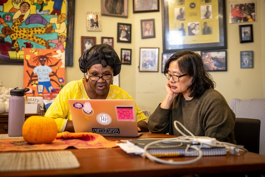 An older Black woman with a middle aged Asian woman in front of a laptop in a home