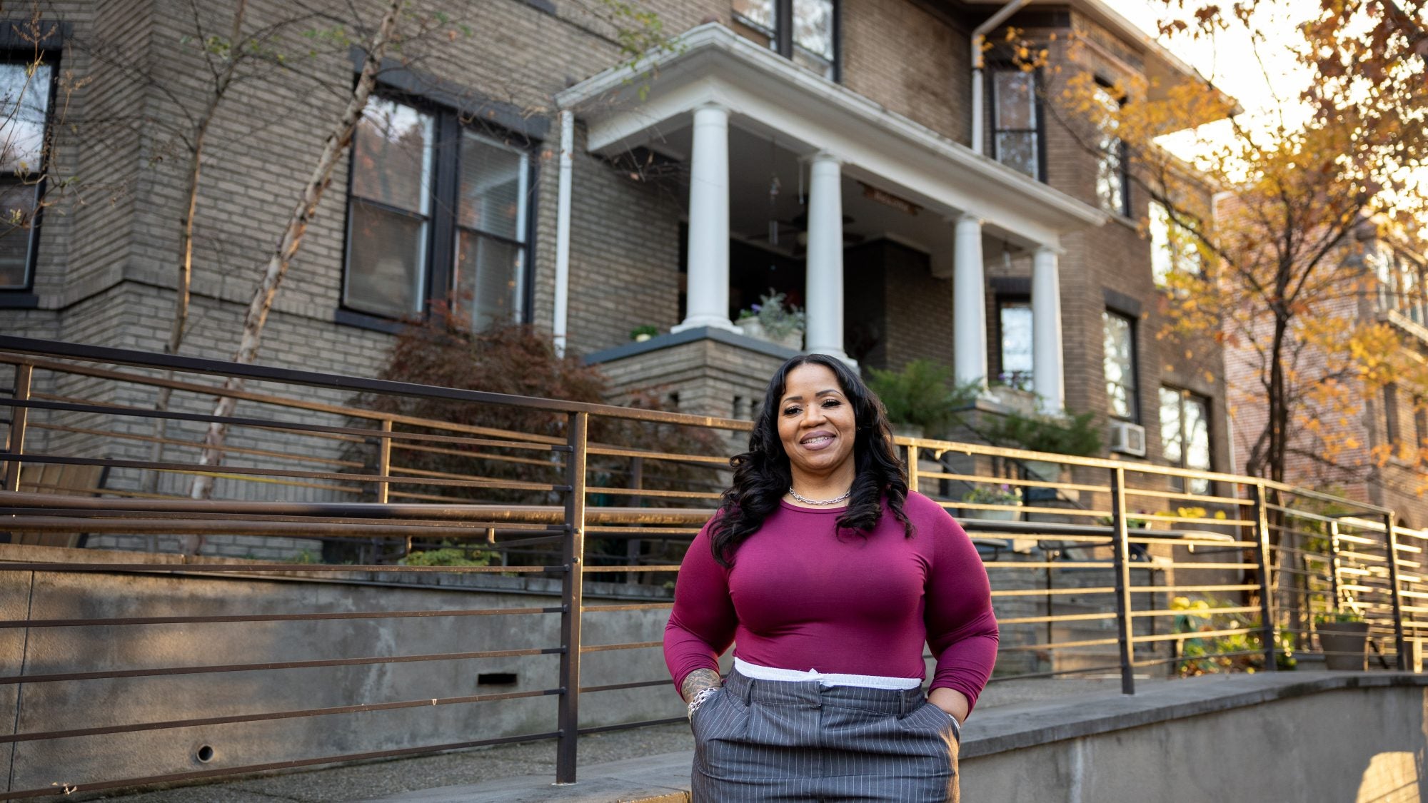 Black woman wearing a purple sweater outside of a row house during golden hour