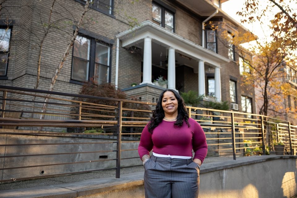 Black woman wearing a purple sweater outside of a row house during golden hour