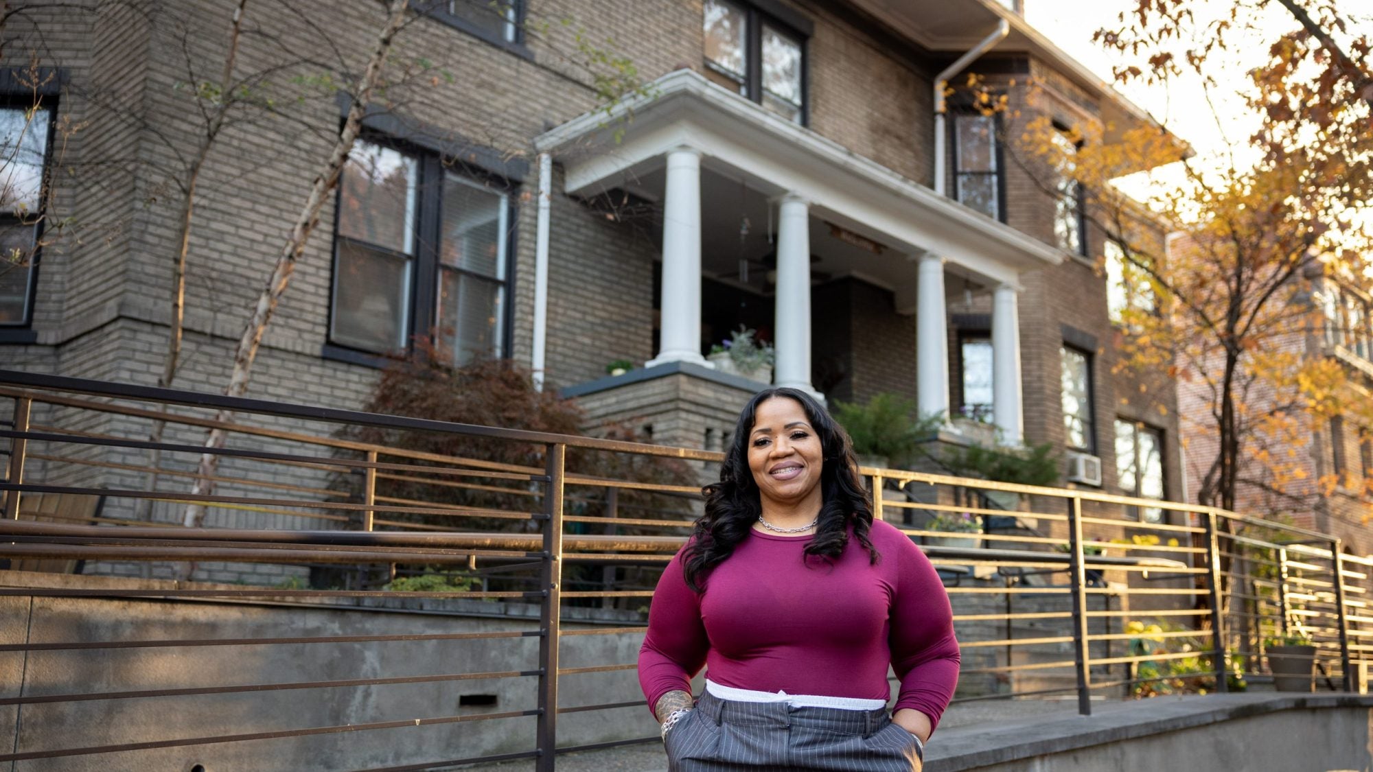 Black woman wearing a purple sweater outside of a row house during golden hour