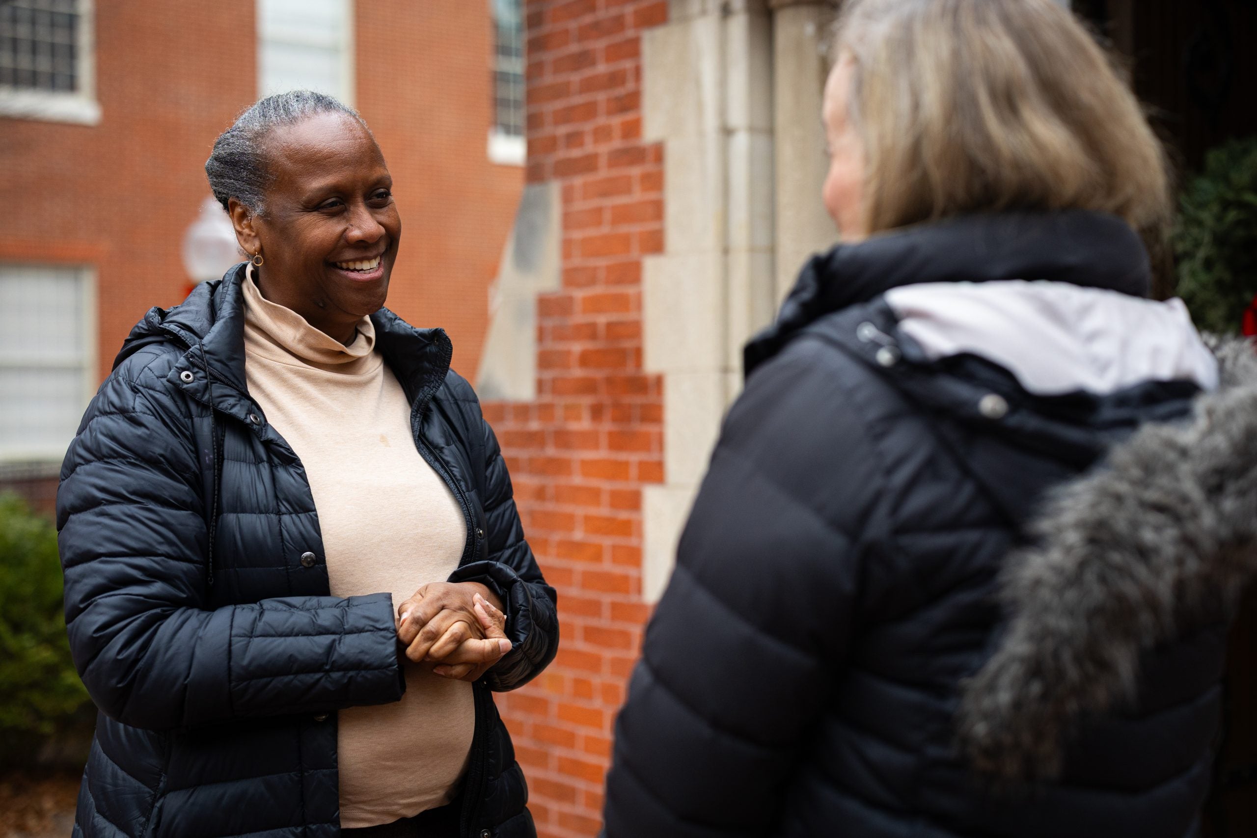 Two women in black winter jackets speak to each other outside a chapel