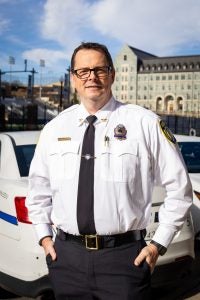 A man in a police uniform stands in front of a cop car
