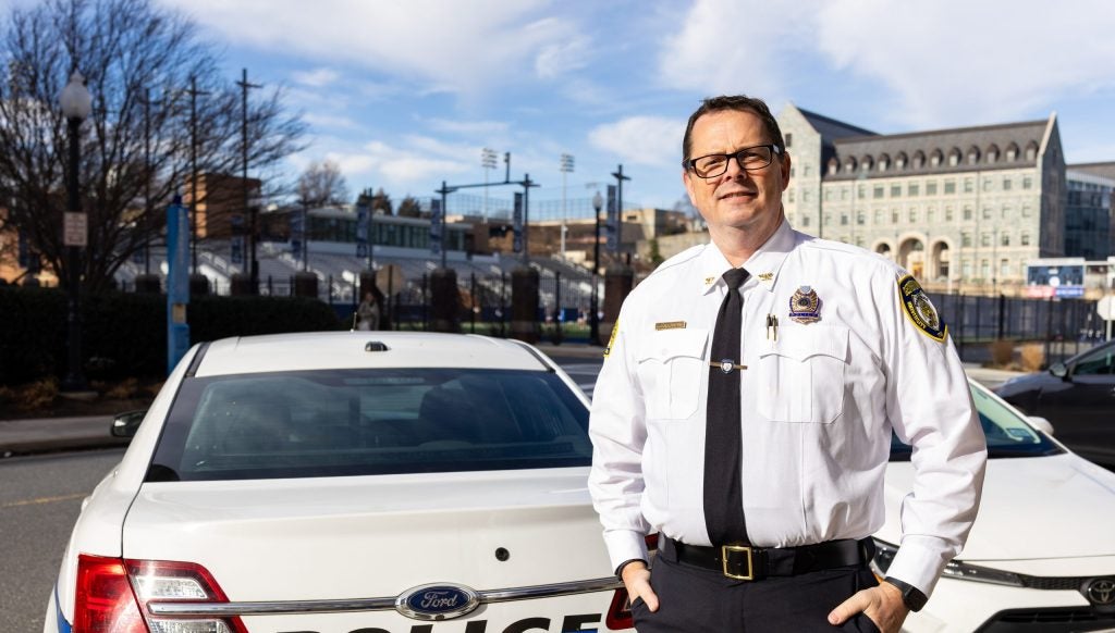 A police chief stands in front of a cop car