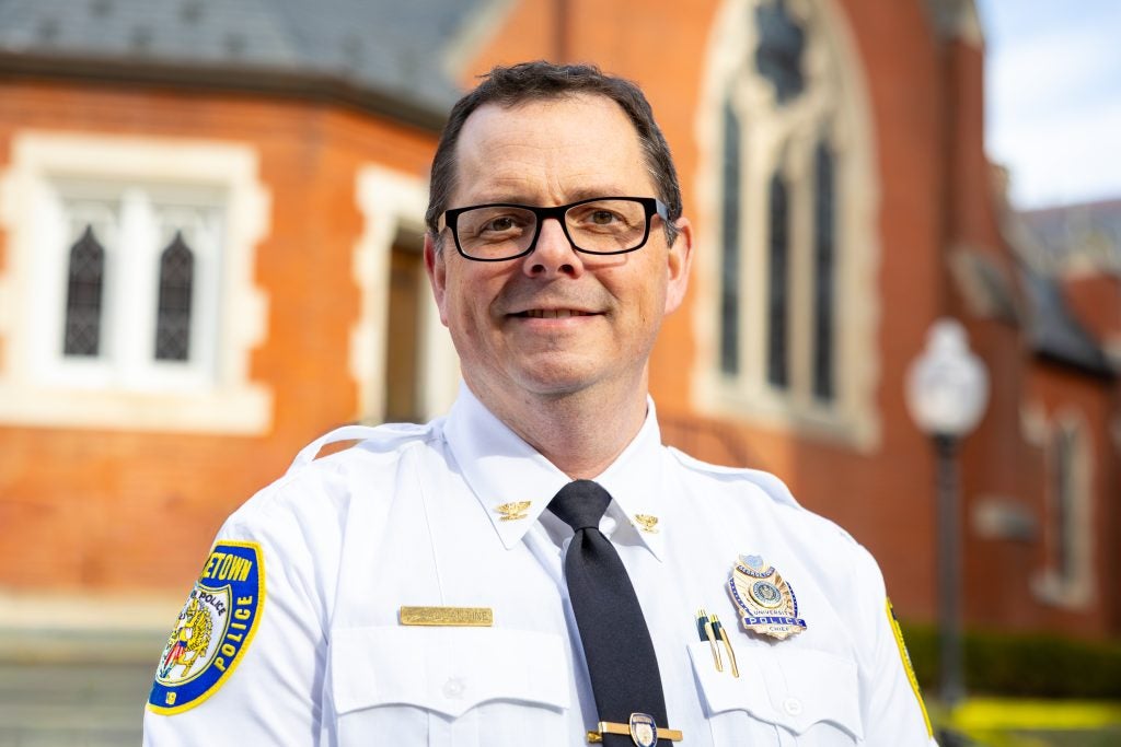 A police chief stands in front of a chapel and smiles