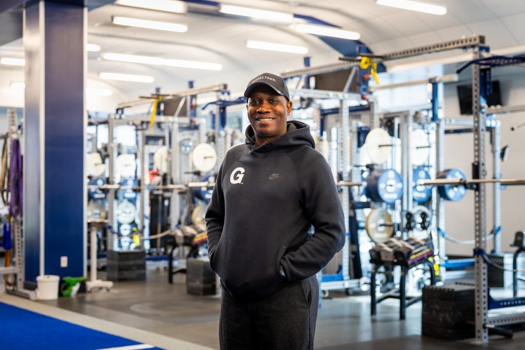 Black man smiling while wearing a Georgetown hoodie and hat
