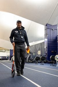 Black man smiling while wearing a Georgetown hoodie and hat and walking along a track