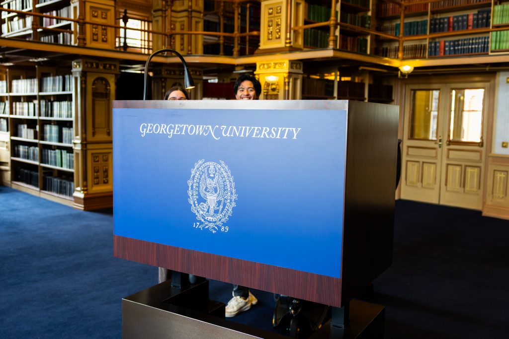 The top of two students' heads peek out from behind an accessible podium that is raised up high.