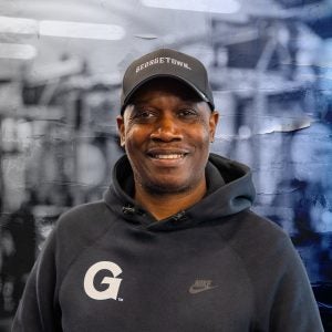 Black man smiling while wearing a Georgetown hoodie and hat smiling