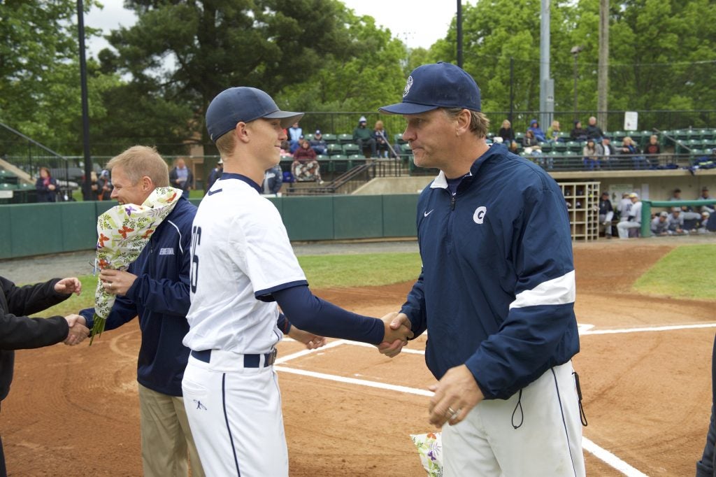 Young man shakes hands with his baseball coach on the field