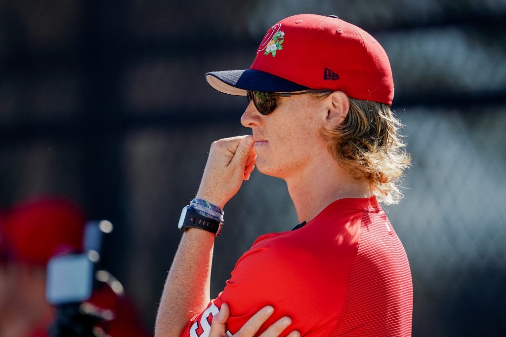 Young man in a red baseball jersey with sunglasses looking toward the baseball field