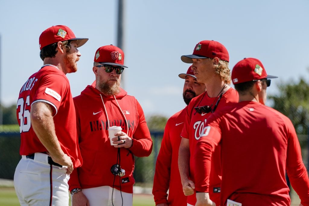 Group of men in Nats uniforms talk on the field on a sunny day