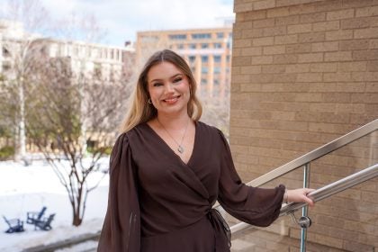 A woman in a brown shirt smiles on a stairway outdoors during the winter.