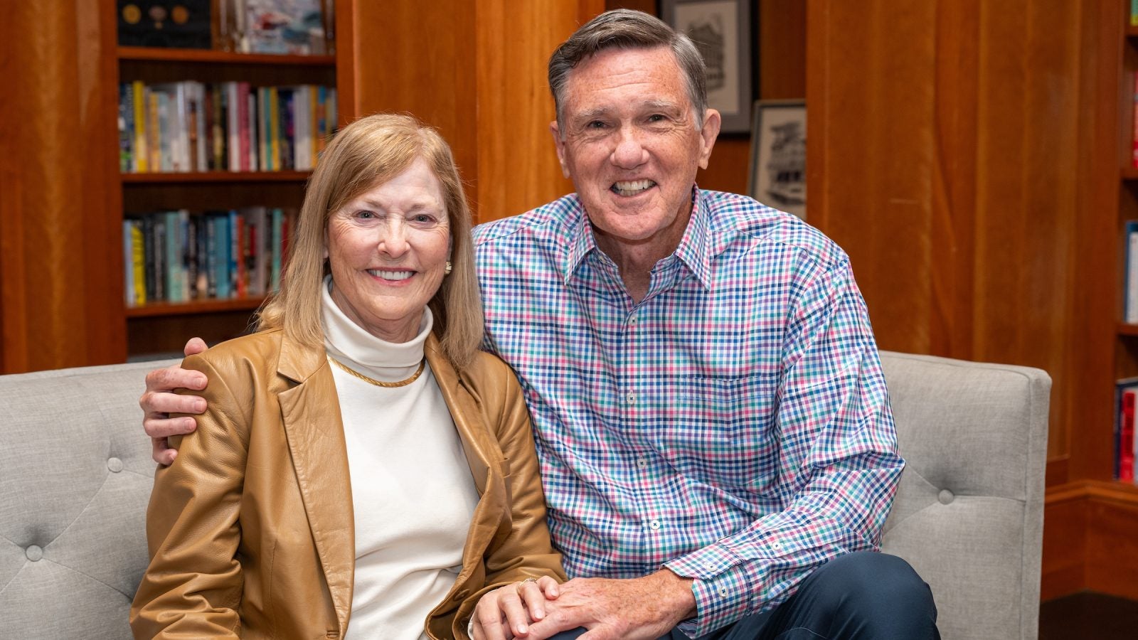 A husband and wife sit and hold each other's hand on a couch.