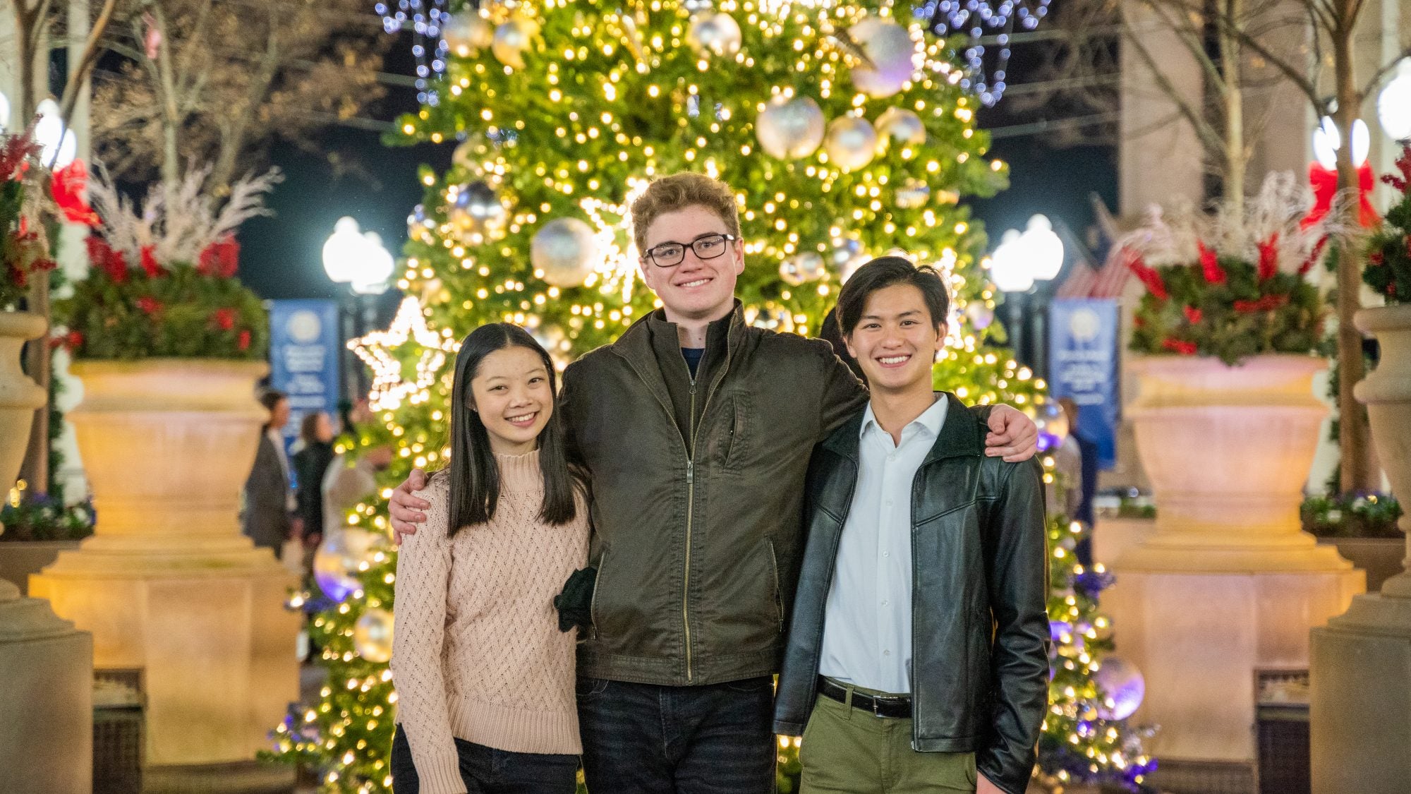 Three college students smiling in front of a Christmas tree
