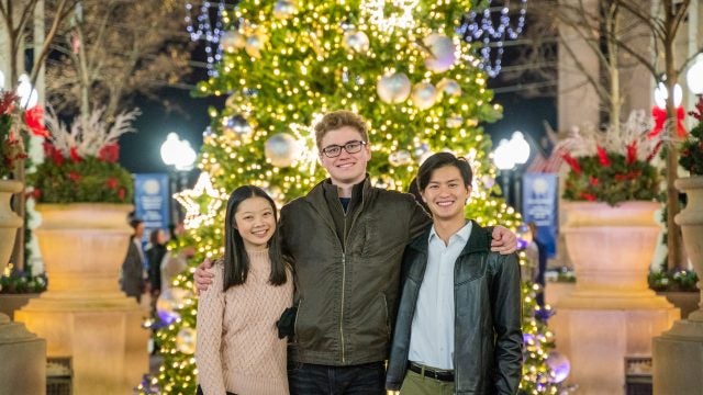 Three college students smiling in front of a Christmas tree