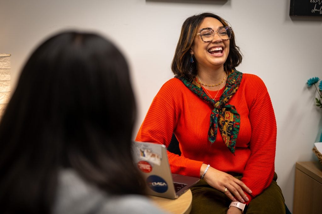 A woman in a red sweater laughs while meeting with a student