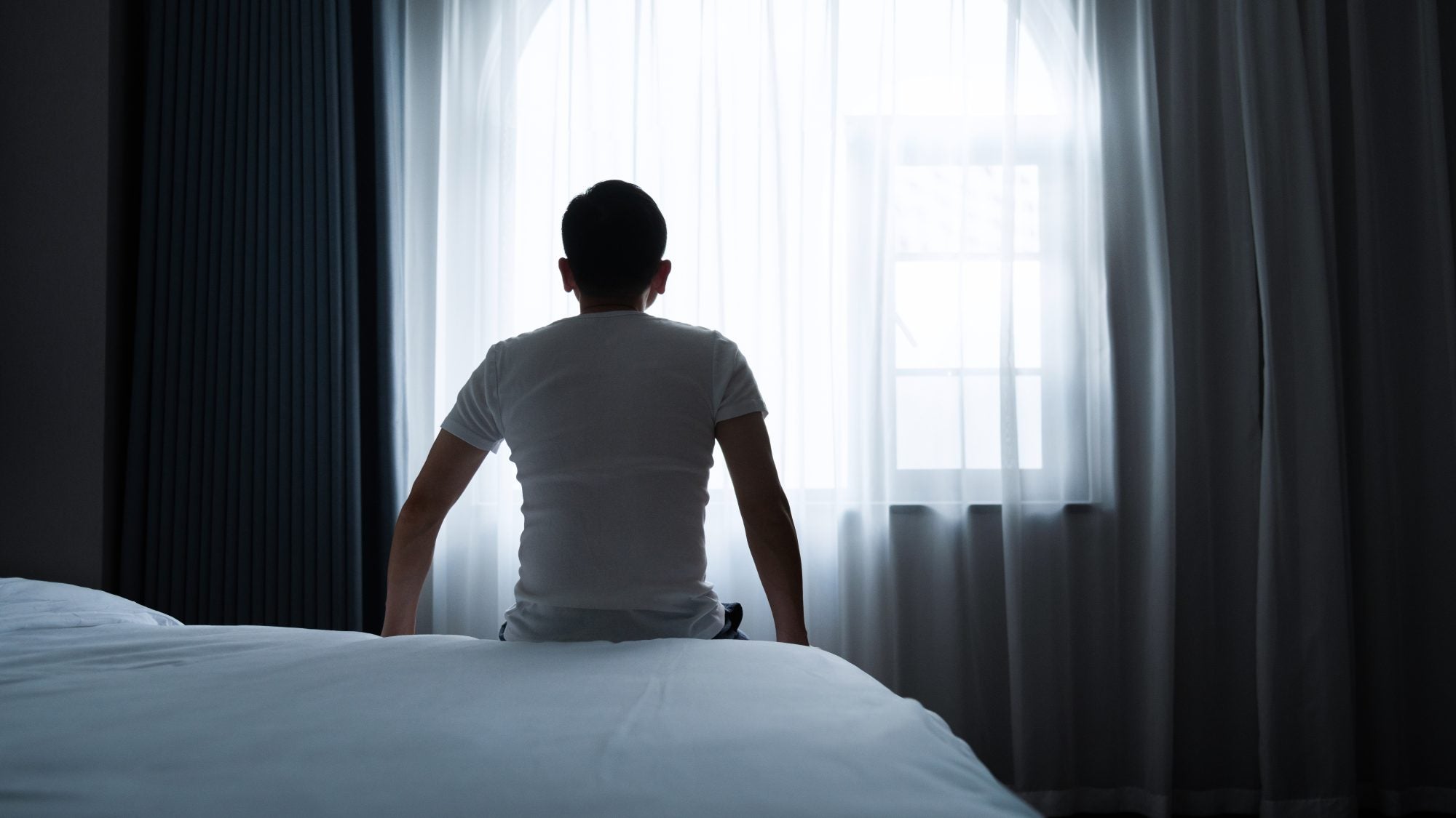 Rear view of a man sitting on bed