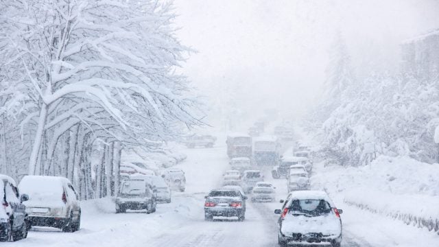 Cars drive on a snowy road during a blizzard