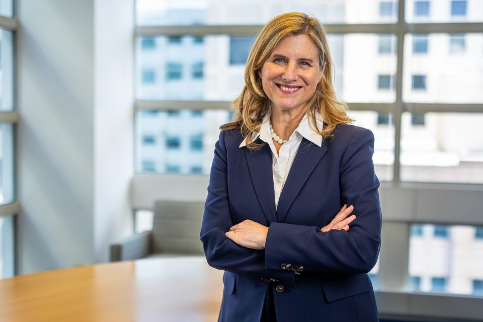 A woman in a blue blazer stands in front of a window