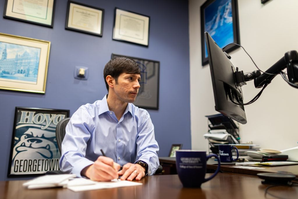A man writes on a legal pad while looking at his computer