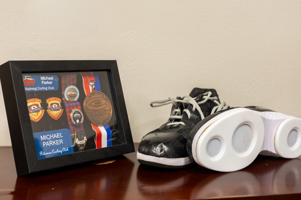 A framed photo of curling medals next to two black curling shoes with white soles