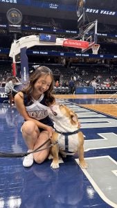 Young Asian woman in a cheer uniform looking at a bulldog on a basketball court