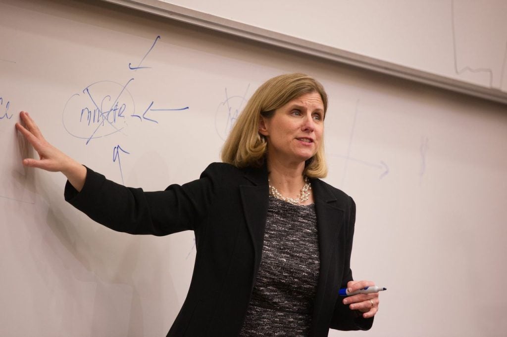 A woman points at a whiteboard while teaching