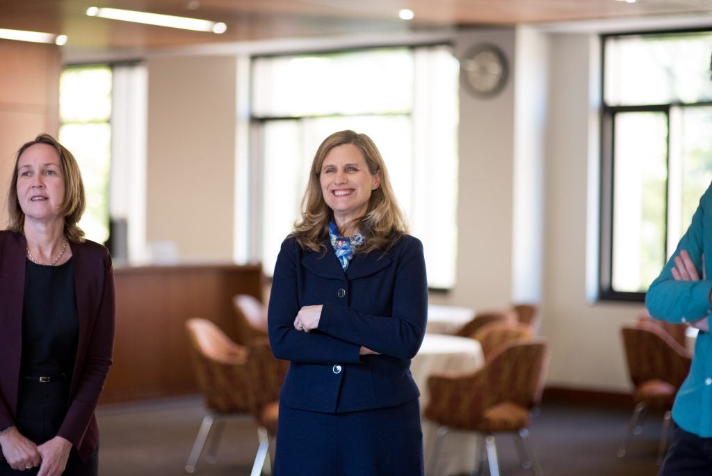A woman smiles with her arms crossed with chairs behind her