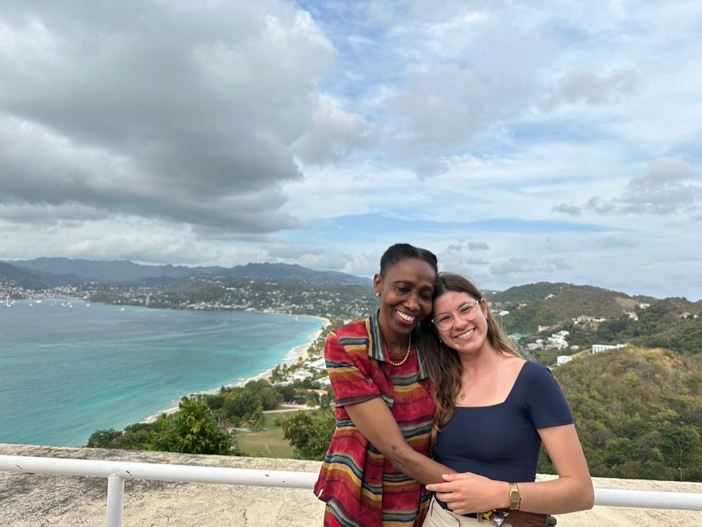Two women pose for a picture in front of a beach