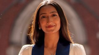 A female student on graduation day wears a blue sash