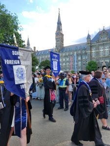 Students dressed in graduation robes and caps process across Georgetown's campus carrying flags