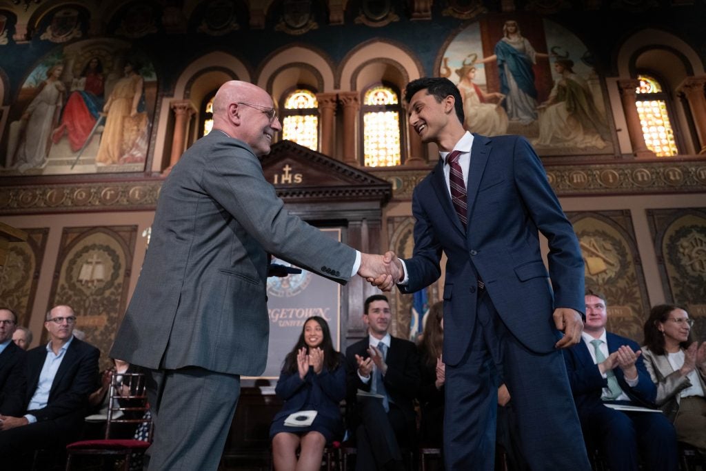 Two men shake hands on a stage in Gaston Hall