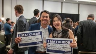 Two students smile and hold up signs of where they matched for their medical residency