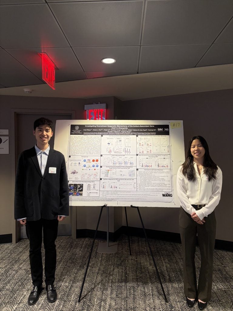 Two students stand in front of a poster that describes their research