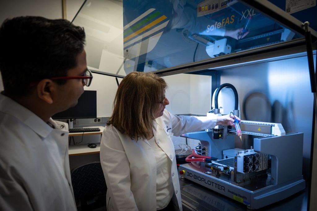Two scientists in white coats interact with a 3d printer