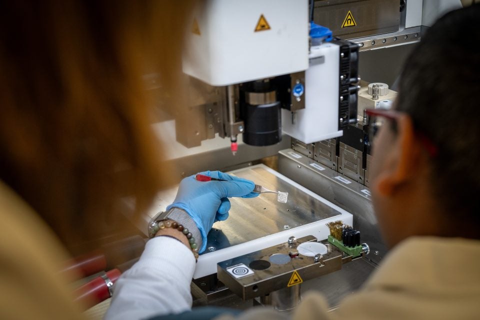 A scientists holds a white square substance with a tweezer by a 3d printer