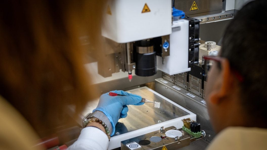 A scientists holds a white square substance with a tweezer by a 3d printer