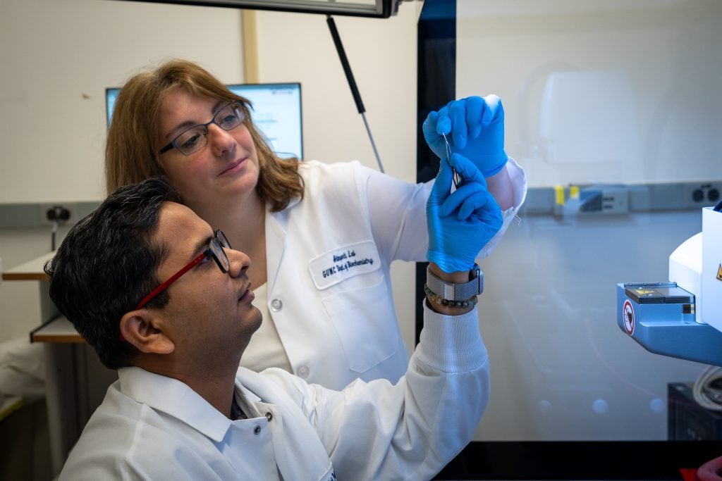 Two scientists in white coats examine a small filament in a lab