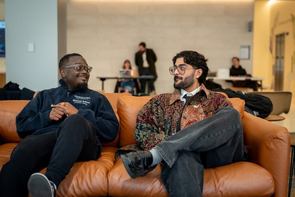 Two male students talk to each other on a brown leather couch