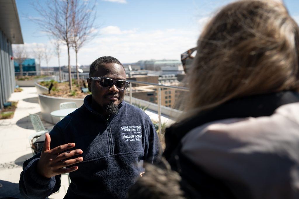 A student in sunglasses speaks to a woman on a balcony