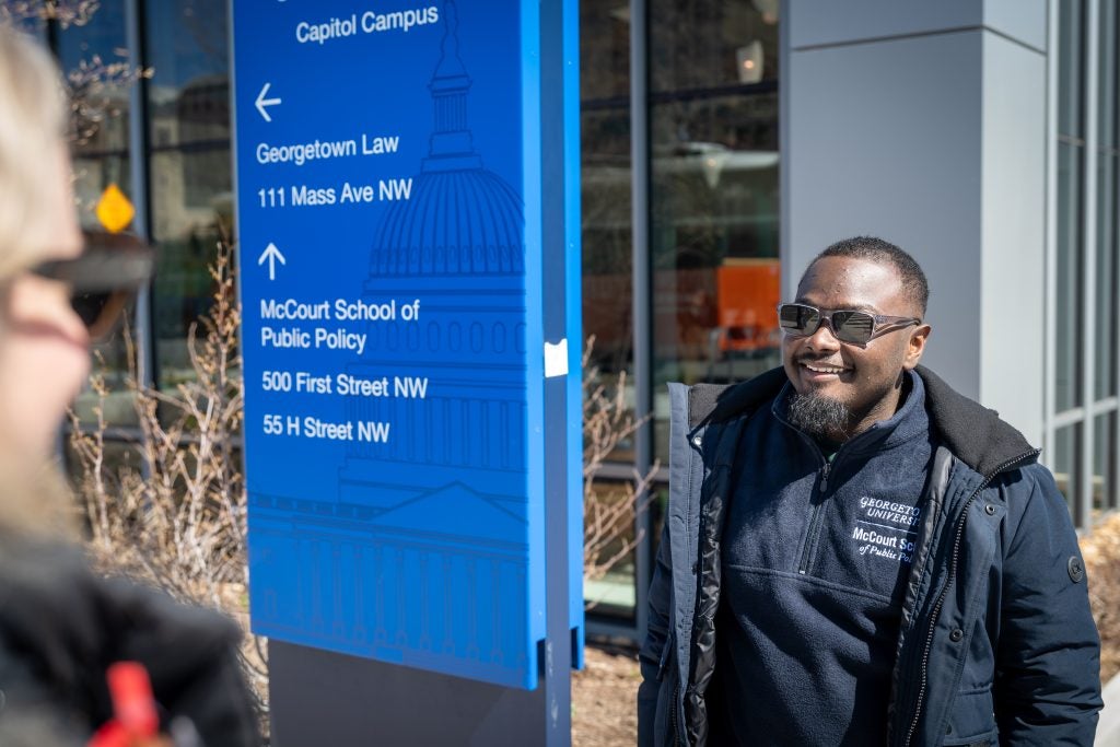 A man talks to a woman next to a guidepost sign with directions on it