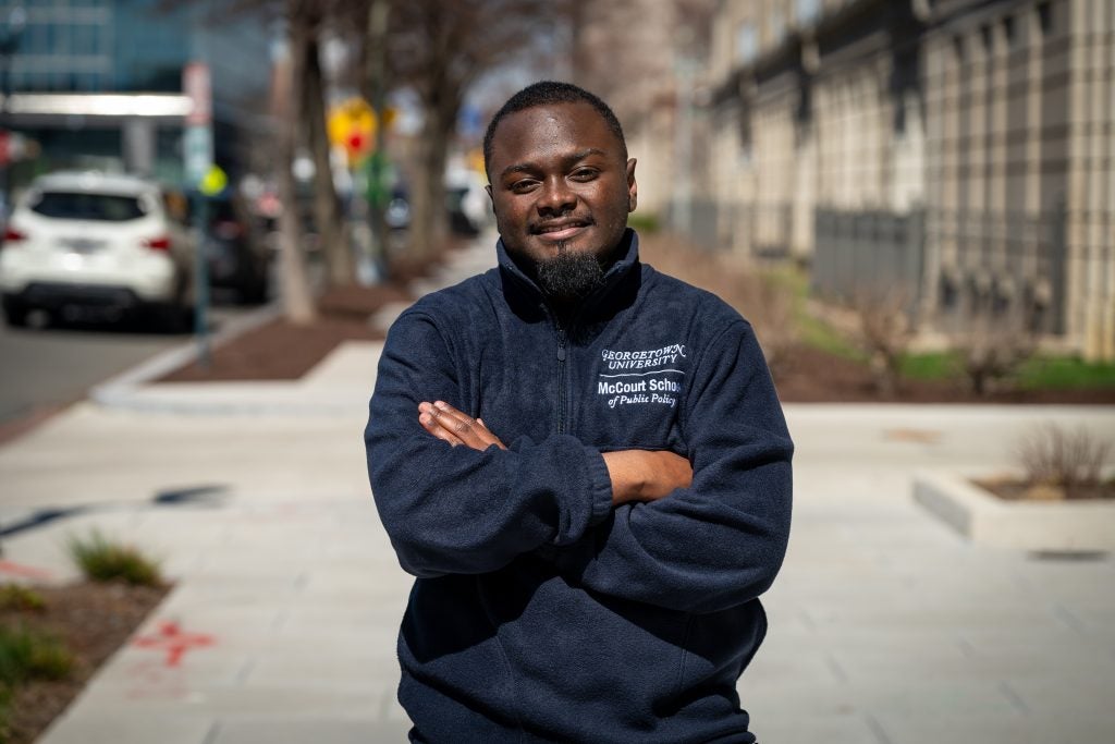 A male student crosses his arms and smiles outside on a sunny winter day.